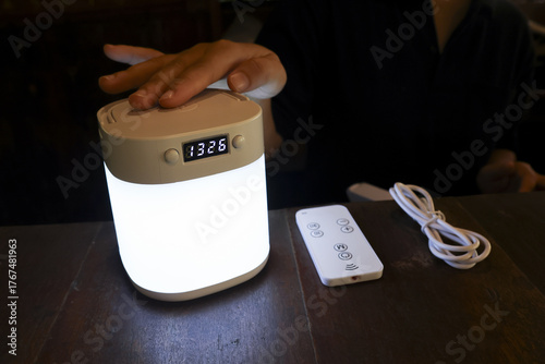 Hand touching glowing portable lamp with digital clock on dark table. cozy night light creating warm, calm, and relaxing atmosphere for peaceful evening at home