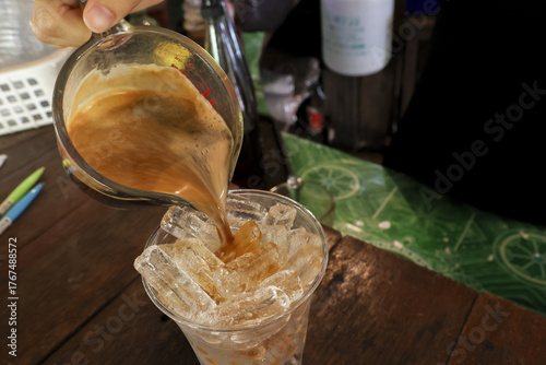 Canvas-taulu Refreshing iced tea beverage pouring from glass into cup of ice at cafe