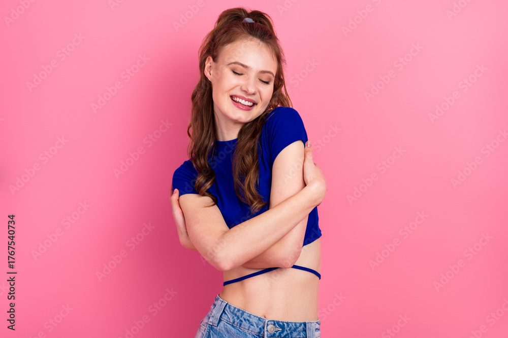 Naklejka premium Young woman in blue crop top and denim expressing joy with a cheerful smile against a vibrant pink background