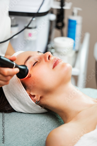 Woman receiving modern ultrasound anti-aging facial treatment in a clinic, esthetician using device for skin tightening and rejuvenation, promoting glowing, youthful complexion