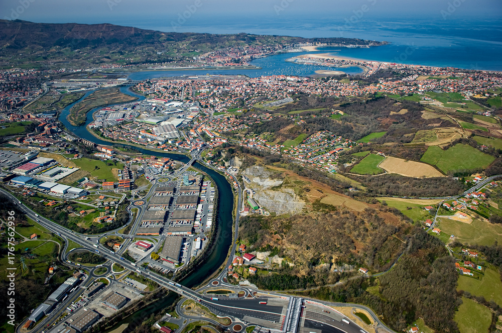 Fototapeta premium The aerial view captures the beautiful landscapes around Peage Biriatou and Hendaye, featuring lush greenery, winding rivers, and a coastal town under a clear blue sky.