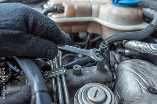 Carta da parati Close-up of a mechanic wearing a glove using a wrench to tighten a bolt on a car engine during vehicle maintenance in a workshop