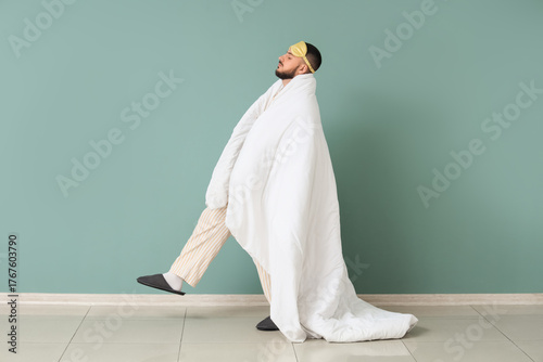 Papier peint Male sleepwalker in pajamas with blanket near green wall