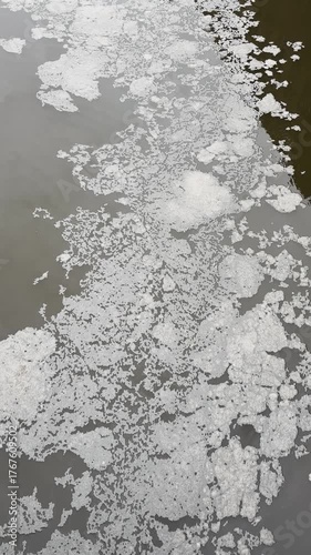 Polluted river water surface with floating foam and debris drifting downstream, captured in Hamburg’s Elbe River.
