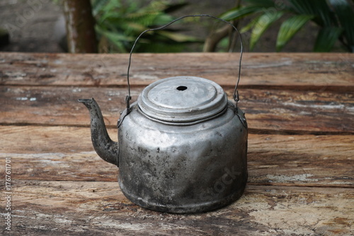 Old and weathered aluminum teapot on a rustic wooden table outdoors.