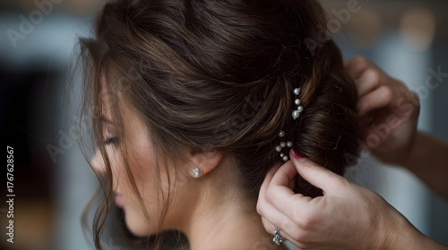 Close up of a woman s elegant brown hair updo being styled with pearl hairpins preparing for a wedding or special event