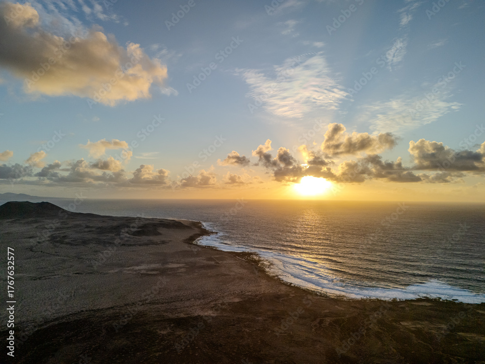 Obraz premium Aerial view of a volcanic cone rising from the arid landscape of La Graciosa Island, Canary Islands, with the Atlantic Ocean in the background. 