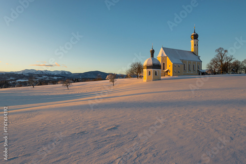 Die barocke Wallfahrtskirche Wilparting im ersten Sonnenlicht bei Sonnenaufgang an einem verschneiten Wintermorgen, Bayern, Deutschland