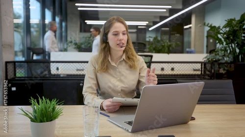 Friendly female helpline operator in call center. Young woman working in call center and holding microphone on headset with hand.