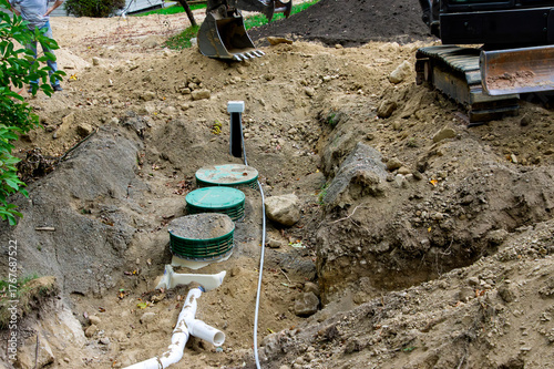 Partially buried treatment tank and UV disinfector with pipe connected, and the drain field in the background at a home septic system installation