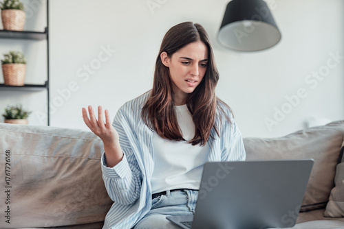 Angry young woman sit on sofa in living room frustrated having operational problems working on laptop, mad millennial girl feel stressed confused with slow internet connection or computer spam
