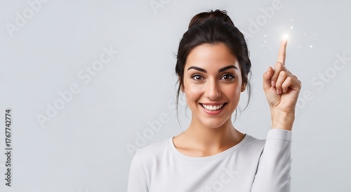 Smiling woman with hair in a bun pointing her finger up with a glowing effect on a light background