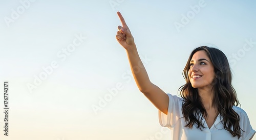 A woman pointing upwards with a smile against a clear bright sky during the daytime outdoors