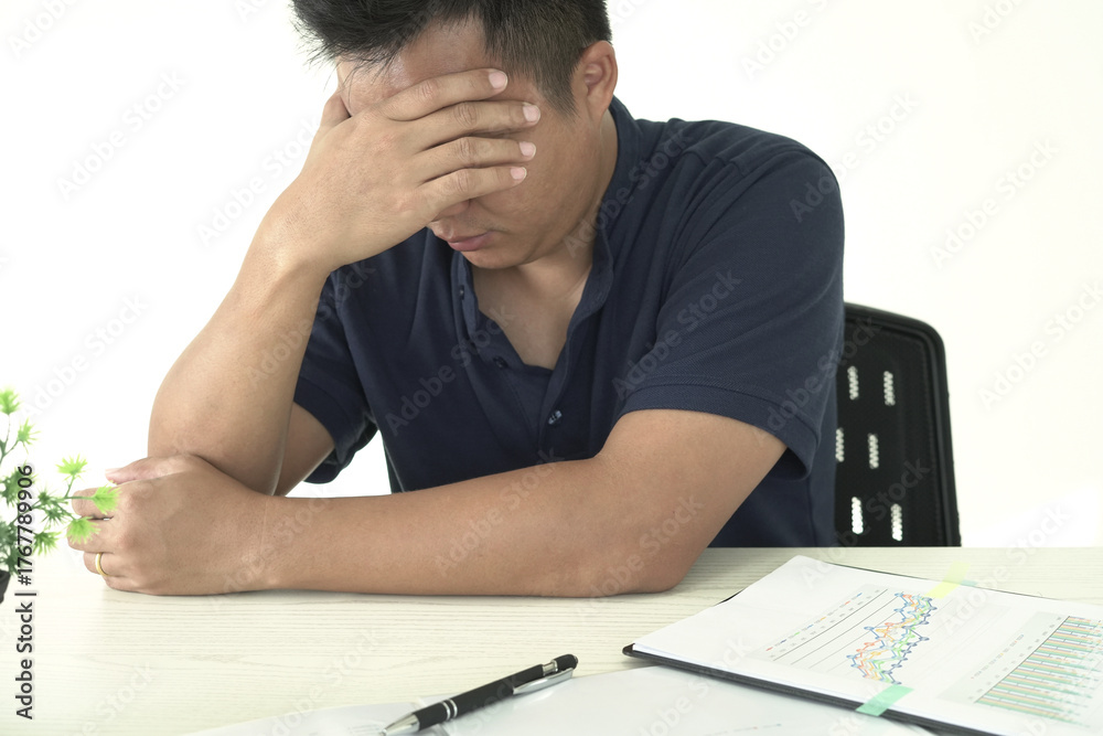 Fototapeta premium An asian businessman is suffering from headache, tension from forehead and getting stress and depression during working, massaging his head, employee life office stress and office syndrome concept. 