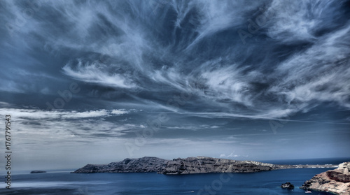View to Thirasia from Oia, Santorini with dramatic cloudscape and contrasting white houses