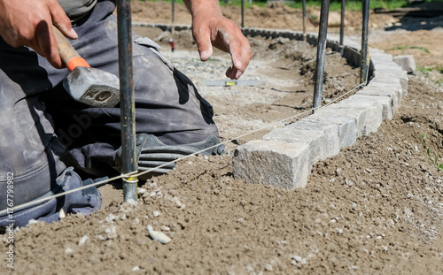 Landschaftsgärtner bei der Arbeit im Detail – präzise Handarbeit im Gartenbau mit Fokus auf Steine, Werkzeug und Struktur. Selektive Schärfe, viel Copy Space