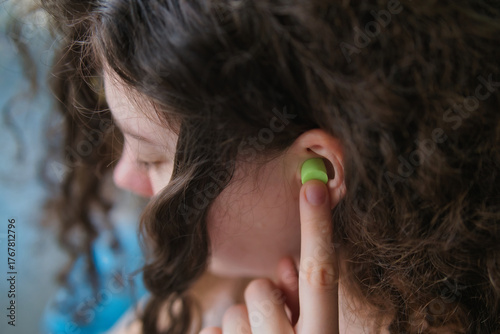 Curly-haired person adjusting wireless earbud while listening to music indoors