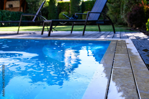 View of the pool edge with active hydromassage creating bubbles and ripples on the water. In the background — lounge chairs on a wooden deck and lush greenery. Cozy and relaxing atmosphere