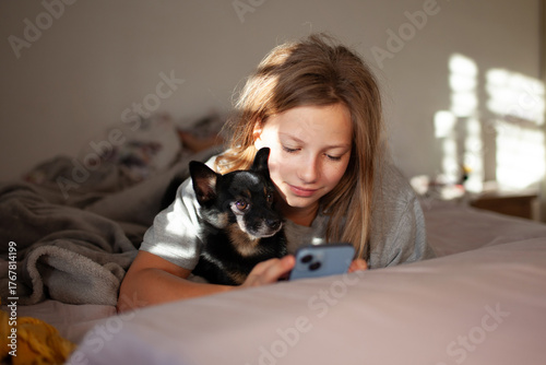 Morning moment — preteen girl with her chihuahua dog in bed using smartphone