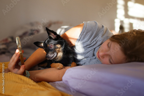Morning moment — preteen girl with her chihuahua dog in bed using smartphone