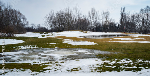 Melting snow in winter landscape with puddles and bare trees