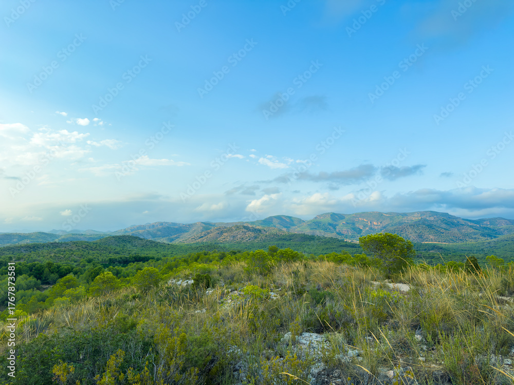Obraz premium Breathtaking view of rolling hills and green valleys under a bright blue sky in the serene landscape of a tranquil natural setting