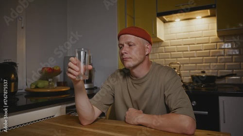 A man sits at the table with a relaxed posture in a cozy minimalist kitchen. The shot highlights home comfort, evening calm, and balanced lifestyle. High quality 4k footage