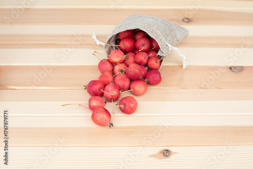 Apples. The fruits of a small-fruited apple tree spilled out of a cloth bag on a light wooden background.