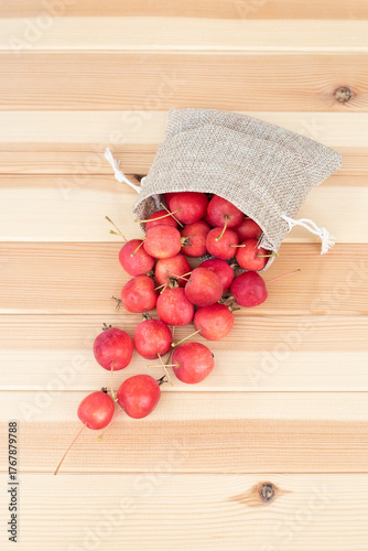 Apples. The fruits of a small-fruited apple tree spilled out of a cloth bag on a light wooden background.