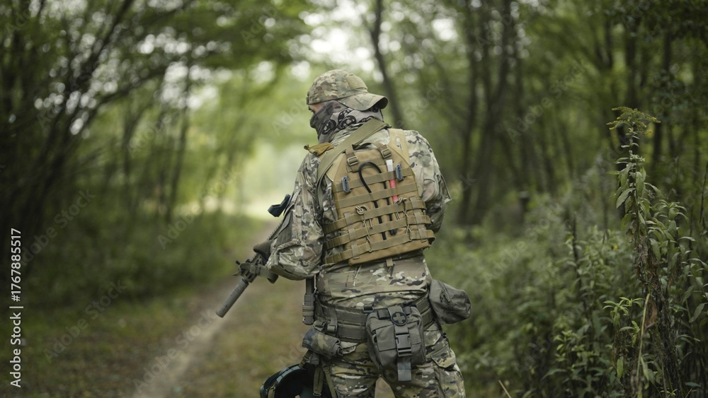 Obraz premium Camouflaged army soldier with AR15 carbine on a mission. Sneaking through a thick green forest. Military recon