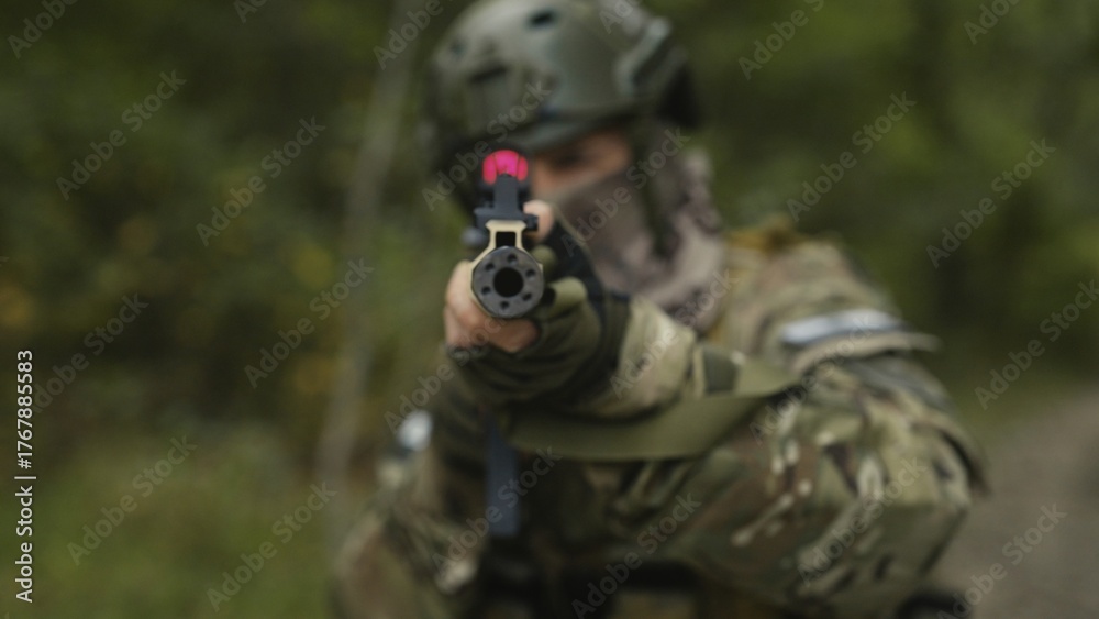 Fototapeta premium Camouflaged and masked soldier with AR15 carbine. Rifle with a collimator aiming at the camera. Selective focus. Military war recon