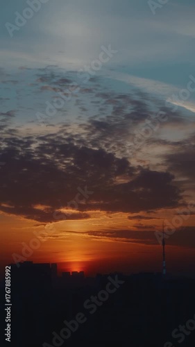 Vertical shot of a city skyline during sunset with warm orange light and textured clouds. Beautiful cinematic view of the evening sky. High quality 4k footage