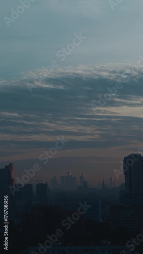 Vertical shot of a large city skyline after sunset, wrapped in soft blue tones and atmospheric haze. Calm and cinematic twilight mood. High quality 4k footage