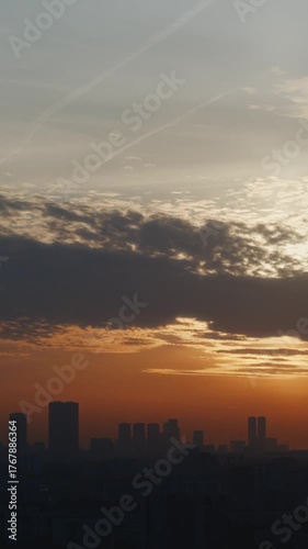 Beautiful sunset over the city skyline with tall buildings on the horizon. Warm orange light breaks through the clouds, creating cinematic depth. High quality 4k footage
