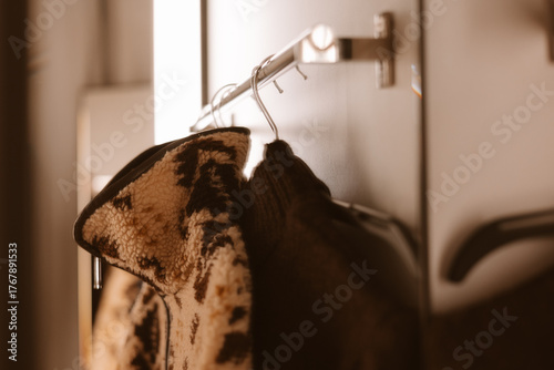 Cozy jacket hanging on a metal rack in a modern interior. A warm fleece jackets hang on a rack, ready for wear, in a sepia-toned room. Warm seasonal clothes in a wardrobe. Warm lighting.