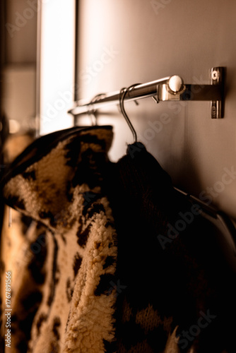 Cozy jacket hanging on a metal rack in a modern interior. A warm fleece jackets hang on a rack, ready for wear, in a sepia-toned room. Warm seasonal clothes in a wardrobe. Warm lighting.