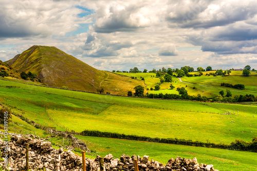 Scenic view of rolling green hills and meadows in the Peak District countryside under dramatic cloudy skies