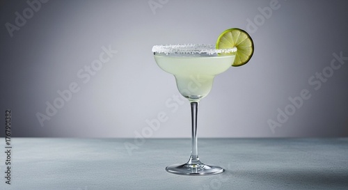 Classic margarita in a stemmed glass with a salt rim and lime wheel garnish, presented on a simple grey surface with a gradient background.