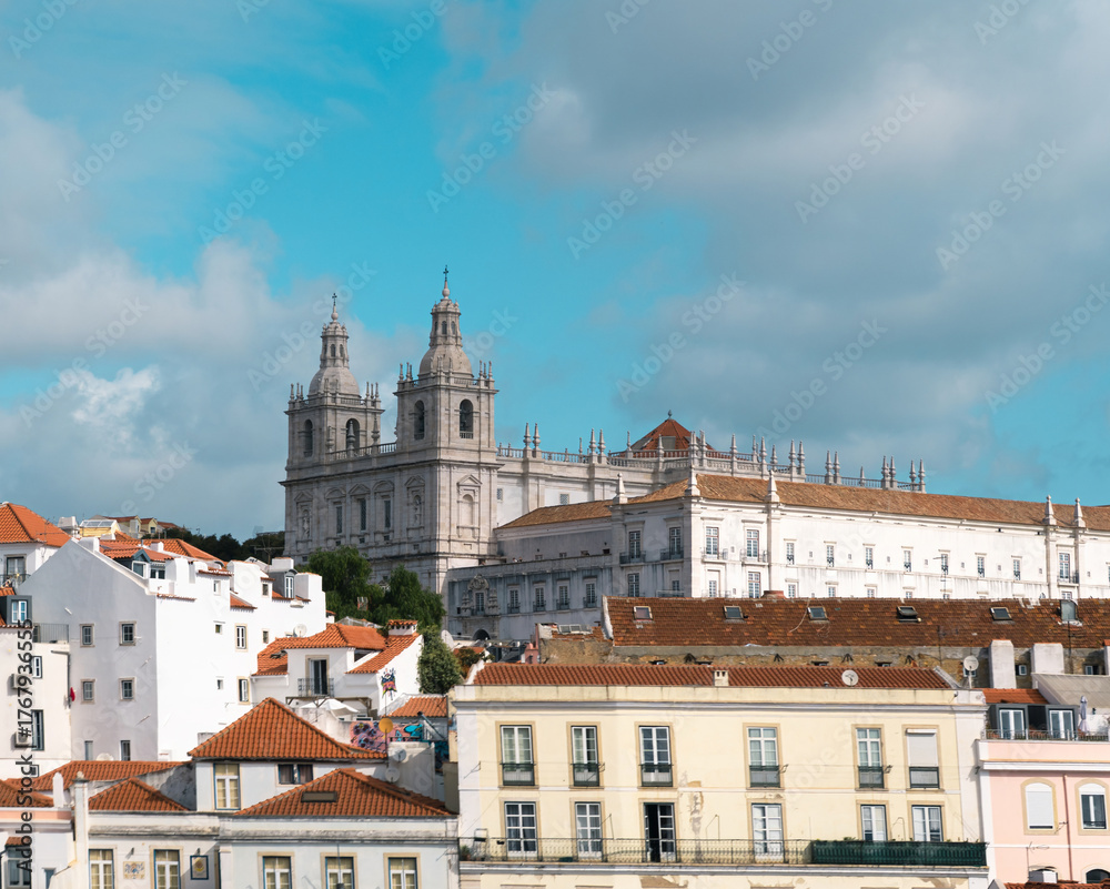 Naklejka premium Historic architecture stands tall over colorful rooftops in Lisbon under a bright blue sky