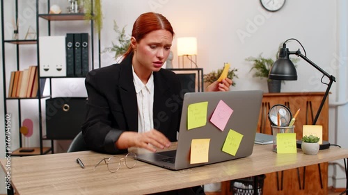 Young businesswoman at home office stares at sticky note covered laptop stressed by piling chores. Freelancer girl at table rips notes away fearing unfinished goals and racing clock before day ends