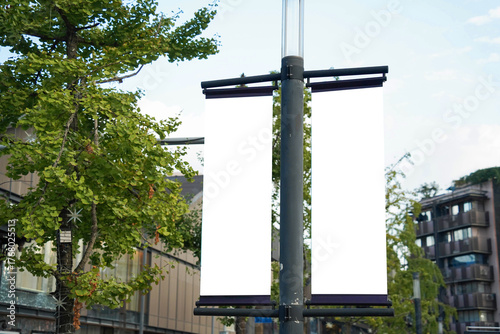 Blank vertical advertising banners double hanging posters by the road, against lush green trees and plants. Mock up.