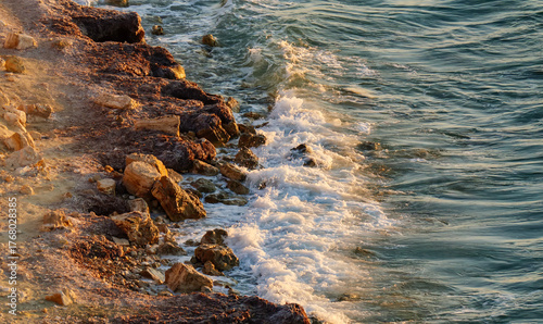 Fototapeta Naklejka Na Ścianę i Meble -  A beautiful vertical shot of a sandy and rocky coastline with gentle sea waves washing ashore during the warm light of golden hour