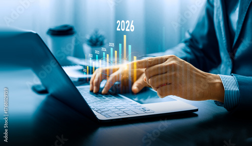 Business growth and financial projection concept for 2026 with businessman analyzing bar chart and data on laptop, showing increasing profit trend, investment success, strategic economic development