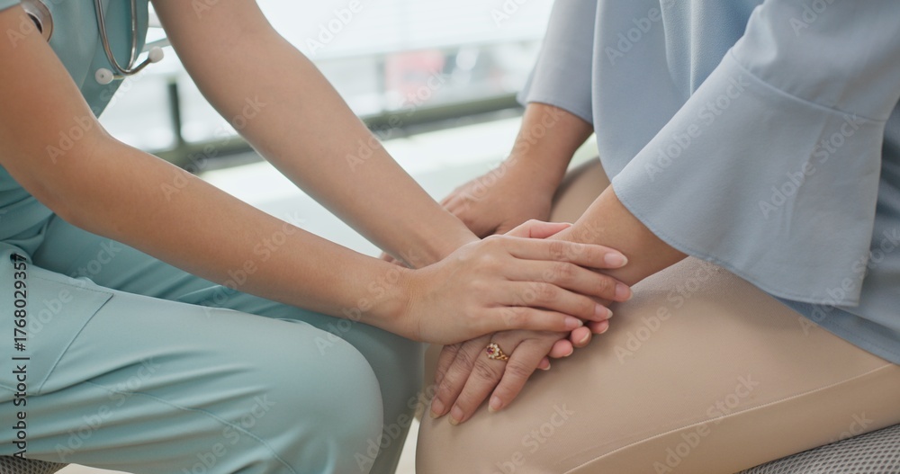 Obraz premium Close up Asian female doctor or nurse gently holds hands and talks with an elderly female patient in a clinic, providing comfort, empathy, and emotional care during a supportive medical consultation.