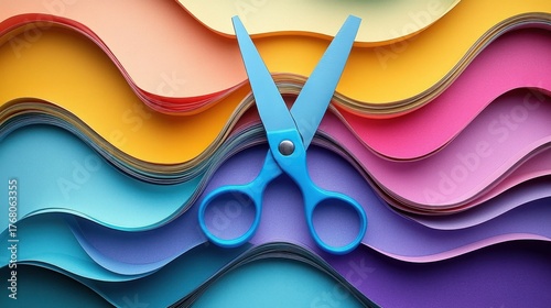 A pair of blue scissors placed on top of colorful wavy layered sheets of paper creating a visually dynamic and vibrant arrangement