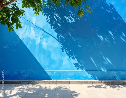 Blue wall with shadows of leaves, sidewalk, and tree, creating a sunny outdoor scene