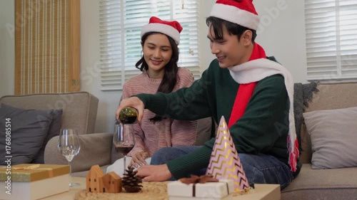 Happy Asian couple celebrating Christmas sharing warmth in winter embrace, exchanging gifts on sofa in cozy home.