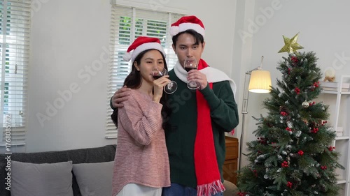 Happy Asian couple celebrating Christmas sharing warmth in winter embrace, exchanging gifts on sofa in cozy home.
