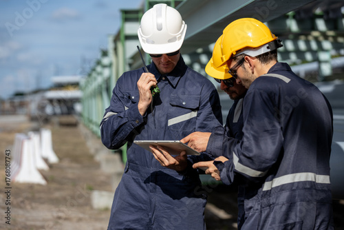 Group of Petroleum engineer in safety uniform discussing project plans using digital tablet checking at pipeline construction site, symbolizing teamwork industrial operations oil refinery.