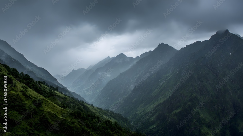 Fototapeta premium Dramatic mountain range descends into a misty, shadowed valley under heavy cloud cover